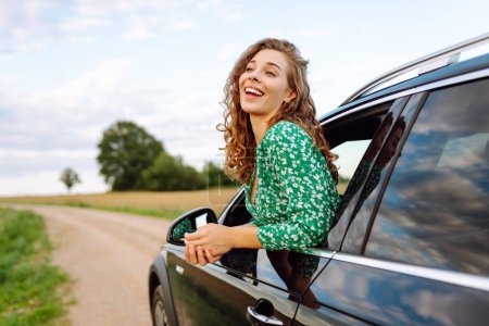 Téléchargez les photos : Femme heureuse tout en sortant par la fenêtre de la voiture en profitant du voyage. Liberté, repos, relax. Voyage en voiture. - en image libre de droit