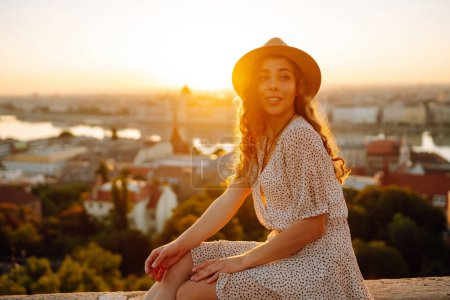 Téléchargez les photos : Portrait de touriste féminine regardant la vue panoramique de la ville au coucher du soleil. Mode de vie, voyage, tourisme, nature, vie active. - en image libre de droit