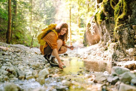Téléchargez les photos : La femme puise de l'eau de source propre dans le ruisseau de montagne. Voyage, aventure. Concept d'un mode de vie actif. - en image libre de droit