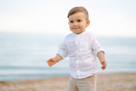 Téléchargez les photos : Petit garçon marche sur la plage en été au coucher du soleil. Bonheur, joie, vacances, plage, concept d'été. - en image libre de droit