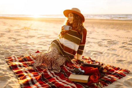 Téléchargez les photos : Jeune femme buvant le café du matin au pique-nique sur la plage. Repos, détente, voyage, concept lifestyle. - en image libre de droit