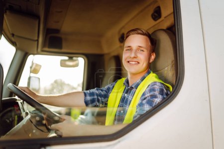Un conductor guapo al volante de un camión en el trabajo. Conductor o transportista en camión y remolque, en un punto de transbordo. Servicio de transporte.