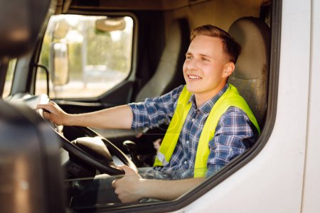 Handsome driver at the wheel of a truck at work. Driver or forwarder on truck and trailer, on a transshipment point. Transportation service.