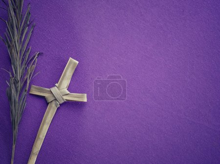Concept chrétien sur Vendredi Saint, Carême et Semaine Sainte. Arrière-plan d'une feuille de palmier sèche et d'une Sainte Croix faite de feuilles de palmier sur fond violet flou.