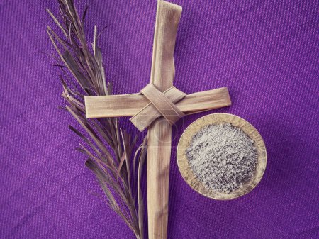 Christianity concept about Ash Wednesday, Good Friday, Lent Season and Holy Week. Holy ash, holy cross made of palm leaf and a dry palm leaf arranged on purple background.