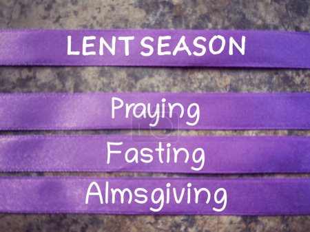 Christianity concept about Ash Wednesday, Good Friday, Lent Season and Holy Week. LENT SEASON, PRAYING, FASTING and ALMSGIVING written on purple ribbons. With blurred background.