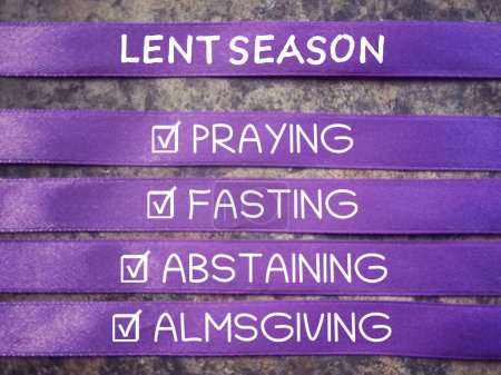 Christianity concept about Ash Wednesday, Good Friday, Lent Season and Holy Week. LENT SEASON, PRAYING, FASTING, ABSTAINING and ALMSGIVING written on purple ribbons. With blurred background.