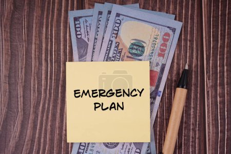 Money and life management concept. EMERGENCY PLAN written on a paper. On background of banknotes.