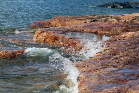 Un montón de pequeñas olas golpeando rocas de playa rojas y negras en Eira aka Eiranranta, Helsinki, Finlandia. Día soleado de verano junto al mar Báltico. Imagen en color que muestra el poder de la naturaleza, el mar y la naturaleza nórdica limpia de la ciudad.