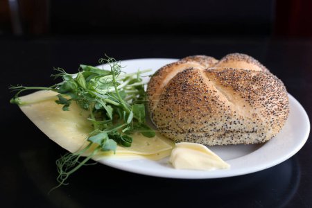 Panes de desayuno en un plato blanco con queso, verduras y mantequilla. Fondo negro. Desayuno sueco, delicioso y saludable. Imagen en color de primer plano.