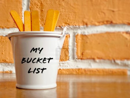 Inspirierend und konzeptionell - Mein Bucket List Text auf einem weißen Eimer mit orangefarbenem Hintergrund. Mit Holzstäben für Kopierraum.