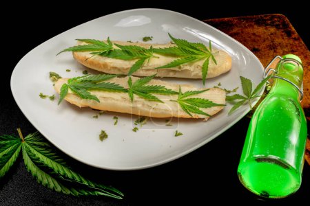 Foto de White plate with butter buns decorated green marijuana Matanuska variety leafs on black table - Imagen libre de derechos