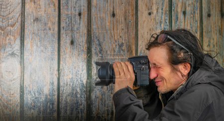 Téléchargez les photos : Homme avec caméra plein cadre noire et lentille grand angle près du vieux mur en bois - en image libre de droit