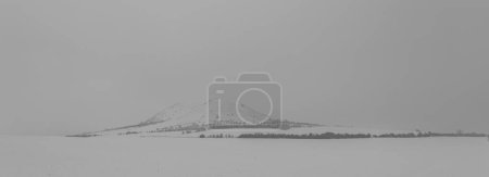 Photo for Rana hill in white storm snowy morning near Louny town and cold meadows - Royalty Free Image