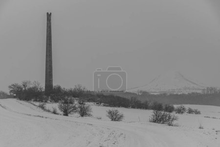 Photo for Rana hill in white storm snowy morning near Louny town with old ruin chimney - Royalty Free Image