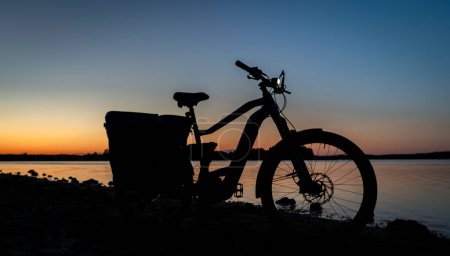 Silhouette of electric bicycle on beach of pond Bezdrev after color sunset