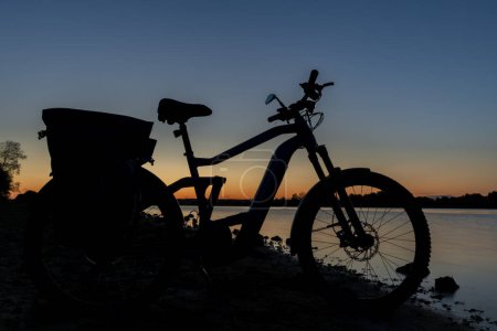 Silueta de bicicleta eléctrica en la playa del estanque Bezdrev después de la puesta del sol de color