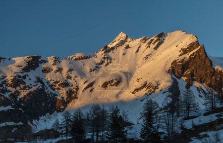 Sunny snowy evening on Simplonpass with blue sky and orange sunny lights