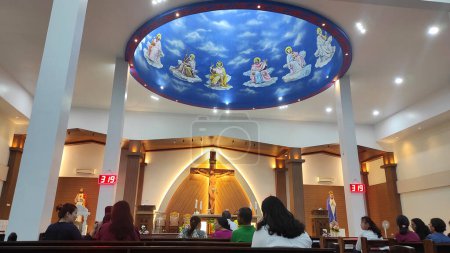 Foto de Pontianak, West Kalimantan, Indonesia - 7 de julio de 2023. El interior de la iglesia contiene cruces y estatuas de María y Jesús. El techo está decorado con pinturas sobre un fondo azul. Había algunas personas celebrando misa.. - Imagen libre de derechos