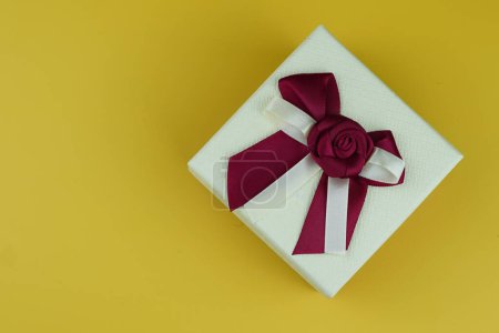 Photo for Gift box with maroon bow on the yellow background as a present in studio isolated - Royalty Free Image
