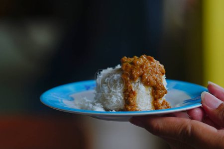 Téléchargez les photos : Riz collant cétan ou indonésien versé avec des ressorts de noix de coco et sauce épicée aux arachides. Vue latérale. Tenez à la main - en image libre de droit