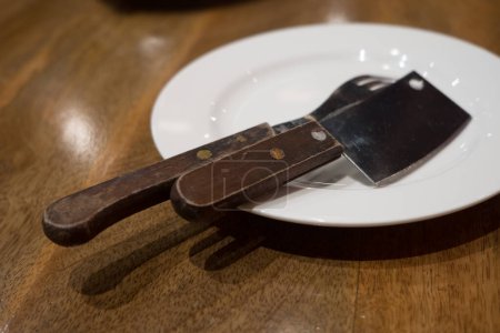 Photo for Fork and knife are put on a white plate served on the wooden table - Royalty Free Image