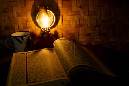 Photo for Holy Quran on the wooden table with vintage traditional kerosene lamp and woven bamboo as background. Studio shot with long exposure. Defocused. - Royalty Free Image