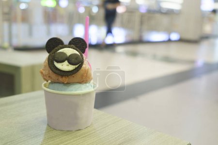 Photo for A cup of gelato with mouse-like biscuit topping served on the wooden table with blurred background. - Royalty Free Image