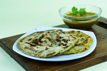 Foto de Roti canai y salsa de curry en plato blanco con servido en la tabla de cortar de madera. Aislado sobre blanco. - Imagen libre de derechos