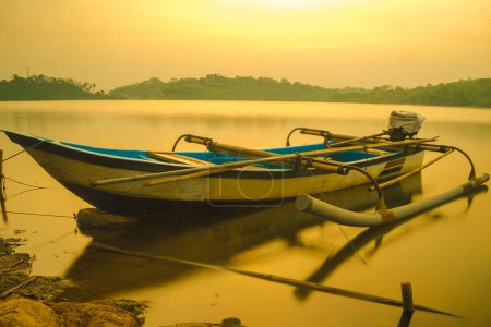 Photo for Traditional boat moored on the calm and tranquil lake during sunrise in Jatibarang Dam, Semarang, Indonesia. Long exposure photography. - Royalty Free Image