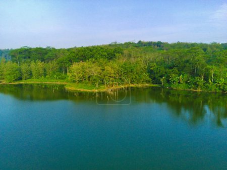 Photo for Aerial footage of a rippling lake with lush green trees, plants and homes at Lembah Jaibarang, Semarang, Indonesia. Drone photography. - Royalty Free Image