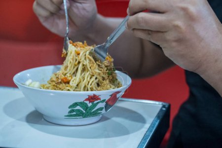 Foto de El primer plano de dos manos se prepara para comer Mie Ayam o popular plato indonesio que consiste en sabrosos y salados fideos de pollo. Fotografía de alimentos. - Imagen libre de derechos