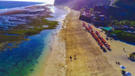 Téléchargez les photos : Une vue aérienne de la plage de Melati, Bali, Indonésie avec des parasols et des personnes. Eau bleue et sable blanc. La plage est bondée, mais elle ressemble à un bel endroit pour se détendre et profiter du soleil et du sable - en image libre de droit