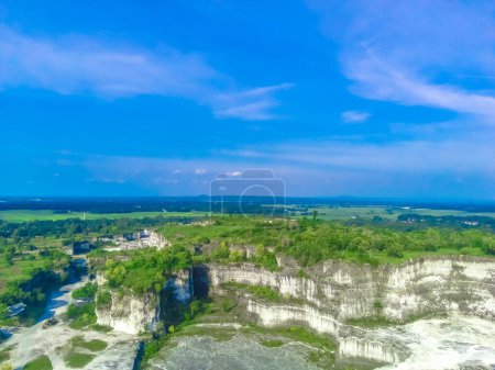 The majestic white limestone cliffs of Bukit Kapur Jaddih in Bangkalan, Madura, Indonesia, with the green vegetations and blue sky.