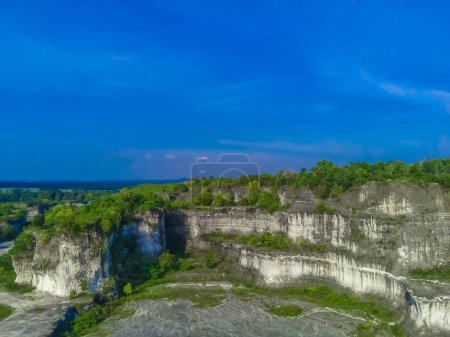 The majestic white limestone cliffs of Bukit Kapur Jaddih in Bangkalan, Madura, Indonesia, with the green vegetations and blue sky.
