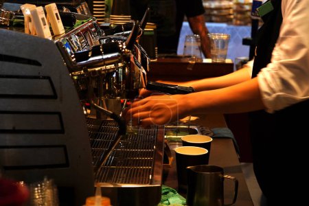 The hands of a barista are preparing coffee using a sophisticated coffee machine that looks expensive and luxurious. The hands picture is motion blurred.
