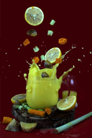 glass filled with a cloudy yellow liquid, with slices of lemon, a knob of ginger, and a piece of turmeric root spilling out of the top