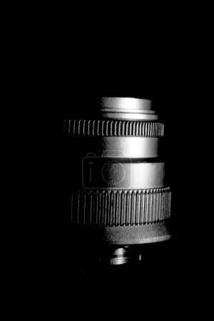 La imagen es un primer plano en blanco y negro de una lente de cámara. La lente tiene varios elementos de vidrio curvado y una carcasa metálica.