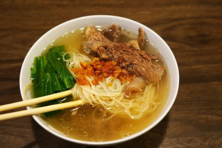 Photo for A bowl of misua or wheat vermicelli with beef tendon. The chopsticks resting on the rim. The noodles are a light brown color. - Royalty Free Image