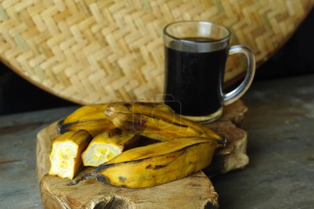 a halved steamed banana and a whole banana on a wooden cutting board next to a black coffee cup.