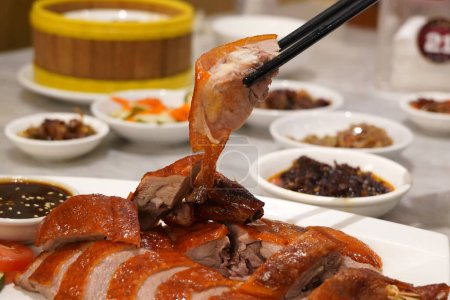 A hand holds chopsticks that grip a piece of Peking duck meat in a restaurant in Surabaya, Indonesia