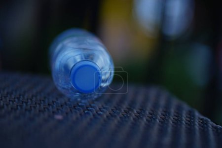 A clear plastic water bottle with a blue cap sits on a brown wooden table with blurred background