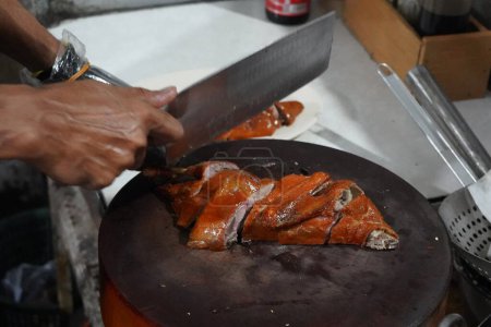 a person chopping roasted duck on a brown cutting board with a silver knife.