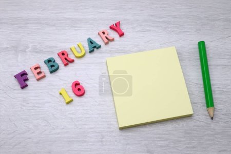 16 de febrero - Calendario diario colorido con notas en bloque y lápiz sobre fondo de tabla de madera, espacio vacío para su texto o diseño 