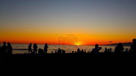 Foto de Atardecer sugerente en la playa con siluetas de personas viendo atardecer - Imagen libre de derechos