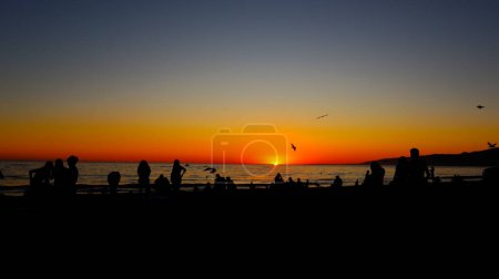 Téléchargez les photos : Coucher de soleil suggestif sur la plage avec des silhouettes de personnes regardant le coucher du soleil - en image libre de droit
