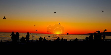 Foto de Atardecer sugerente en la playa con siluetas de personas viendo atardecer - Imagen libre de derechos