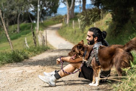 Téléchargez les photos : Adulte métis homme au repos et souriant avec son chien collie frontière au bord de la route en zone rurale - en image libre de droit
