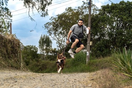 mestizo man with beard jumping and running in rural area with his cheerful border collie dog