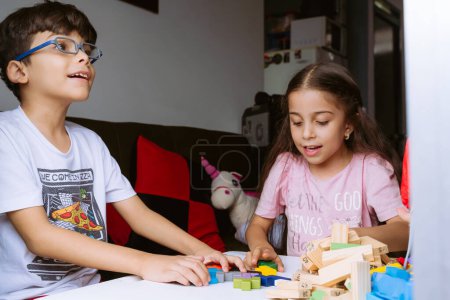 International Children Day. Beautiful Latino children playing with blocks on a white table. Playful, fun and thinking games. Happy children at home.